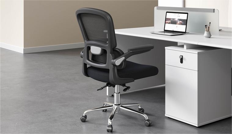An balck office chair with a flip-up armrest in front of the office desk. With a cabinet under the desk